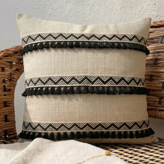 Decorative pillow with black tassels and patterns on a textured surface