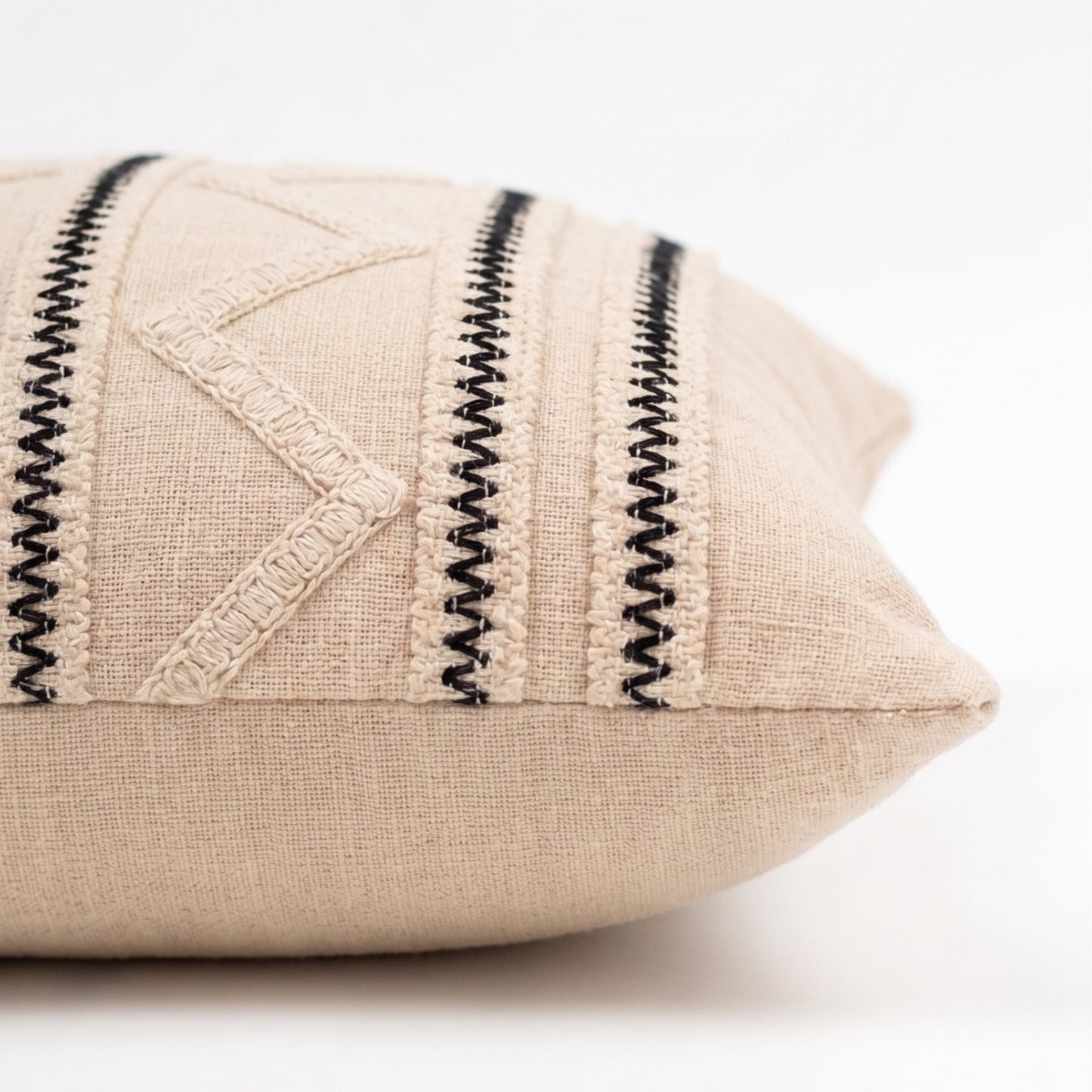Beige pillow with black zigzag stitching on a white background