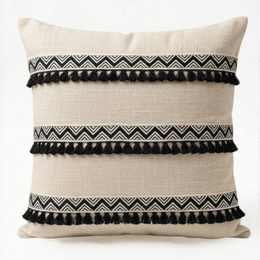 Decorative pillow with black and white zigzag patterns and tassels on a beige background