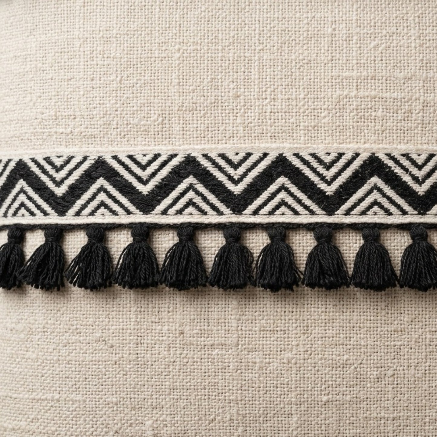 Textile border with black and white zigzag pattern and tassels on a beige fabric background