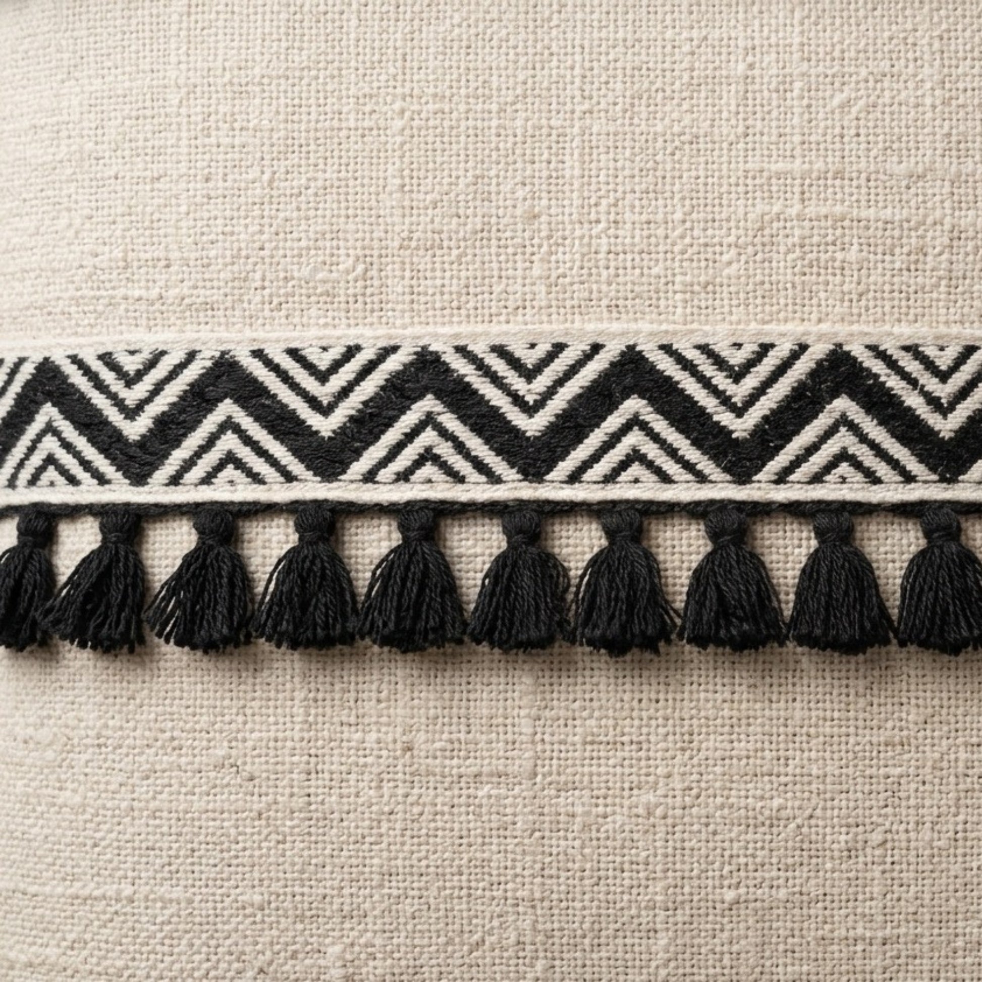 Textile border with black and white zigzag pattern and tassels on a beige fabric background